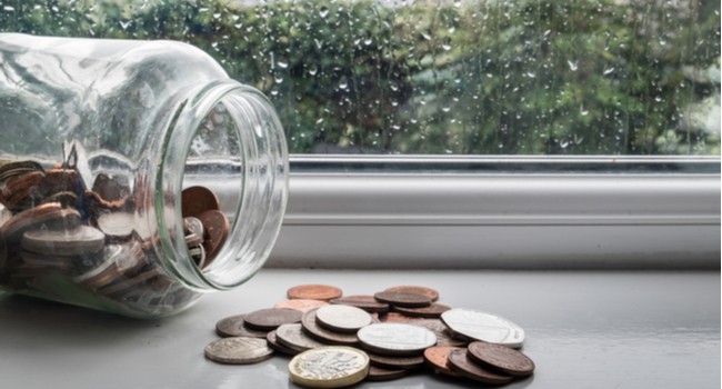 A jar of money tipped over with a rainy day in the background