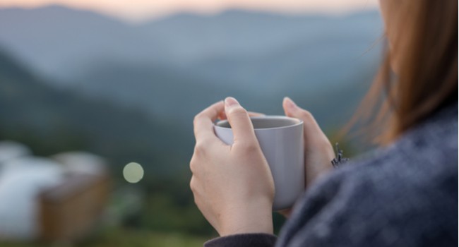 A woman holding a cup of coffee overlooking a green landscape