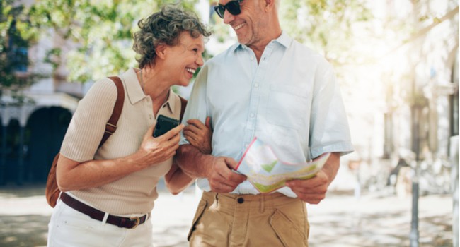 An older couple laughing as they walk around a town with a map