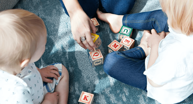 Two young children playing with wooden blocks with their mother
