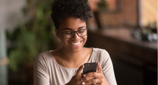 A woman smiling as she looks at her phone screen