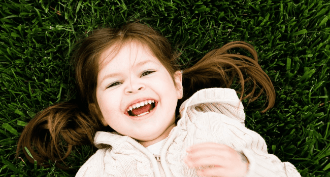 A child laughing as she lays on some grass