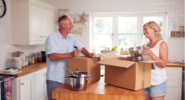 A couple packing items into a box in a kitchen.