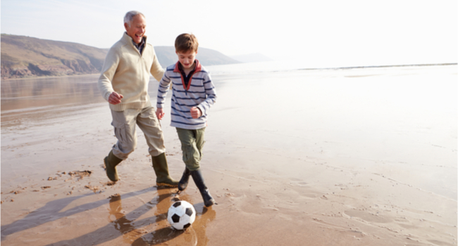 A grandfather and his grandson playing football on a beach.